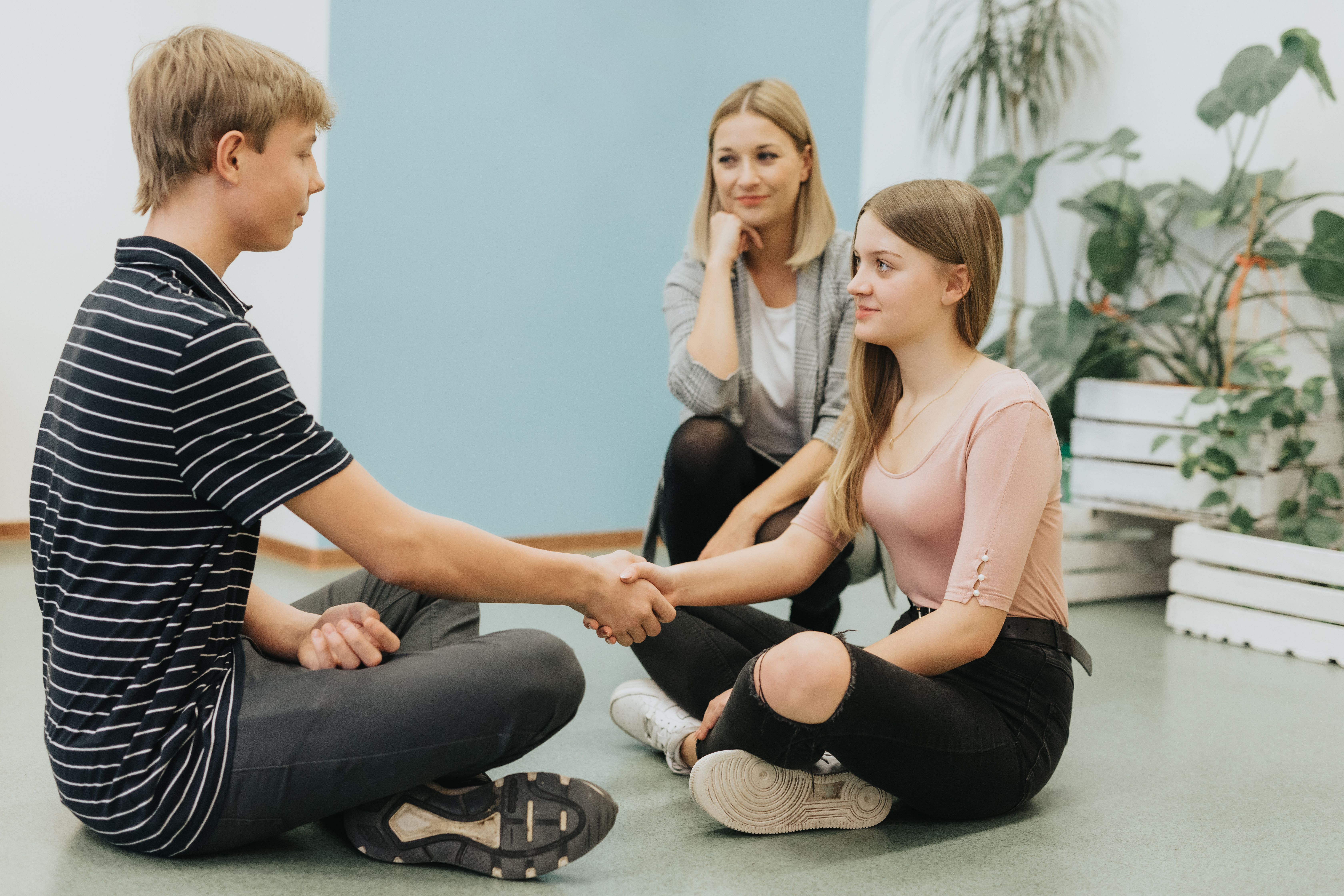 Two friends at odds shake hands during a workshop with a psychologist at school
